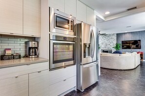 A modern kitchen with stainless steel appliances, a coffee bar, and a living area with a sofa and TV. - Putting Green & Outdoor Lounge! Palm Springs Home (Palm Springs)