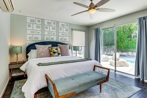 A bedroom with a bed, a bench, a ceiling fan, a nightstand with a lamp, and a view of a swimming pool. - Putting Green & Outdoor Lounge! Palm Springs Home (Palm Springs)