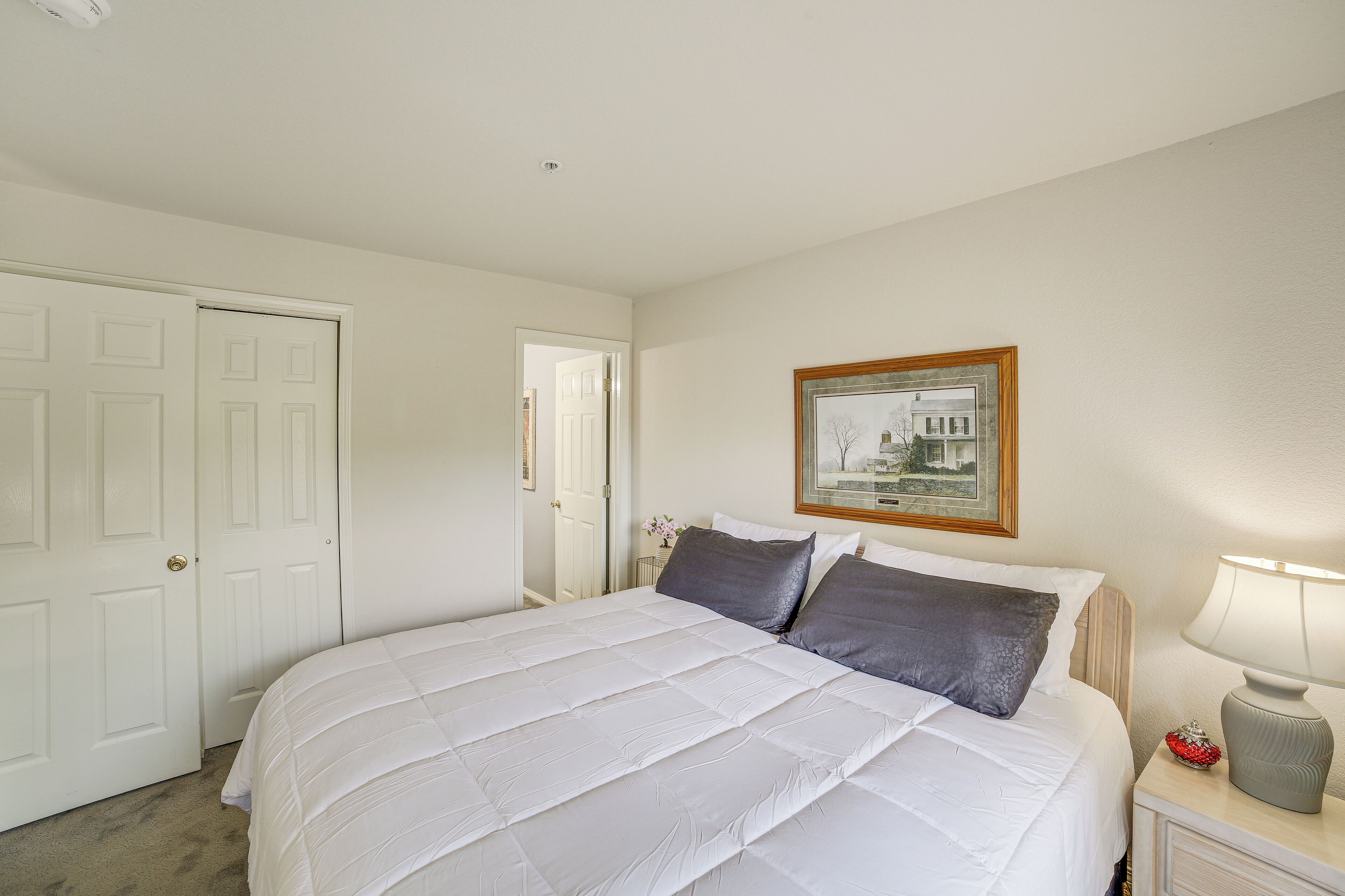 A bedroom with a bed, a nightstand, a lamp, a framed picture on the wall, and a door.