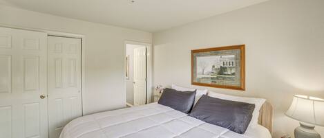 A bedroom with a bed, a nightstand, a lamp, a framed picture on the wall, and a door.
