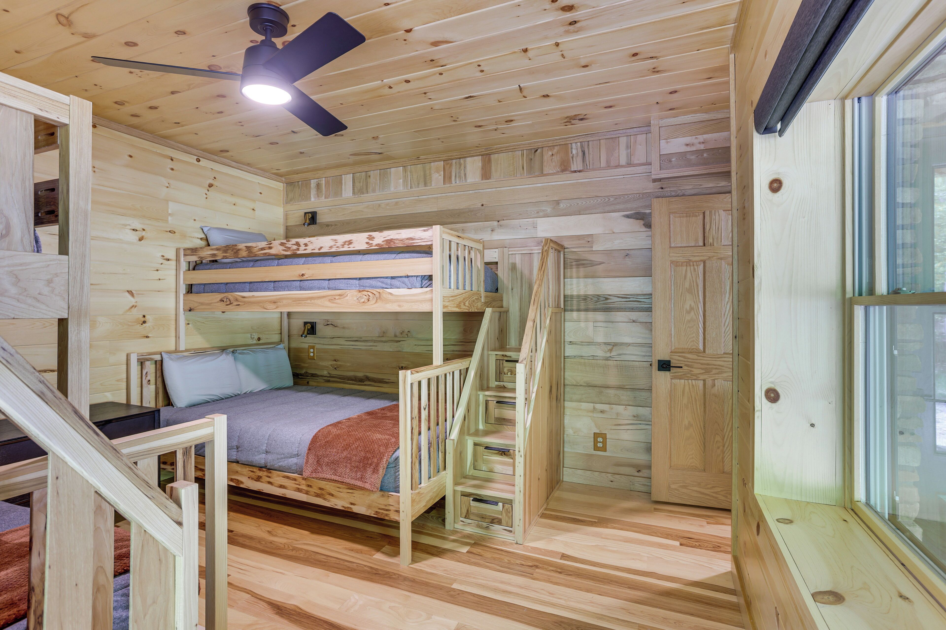 A wooden cabin interior with bunk beds, a staircase, and a window.