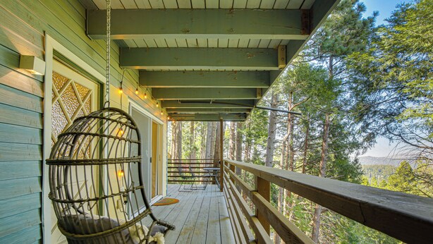 Une terrasse en bois avec un fauteuil suspendu, une balustrade en bois et une vue sur les arbres.