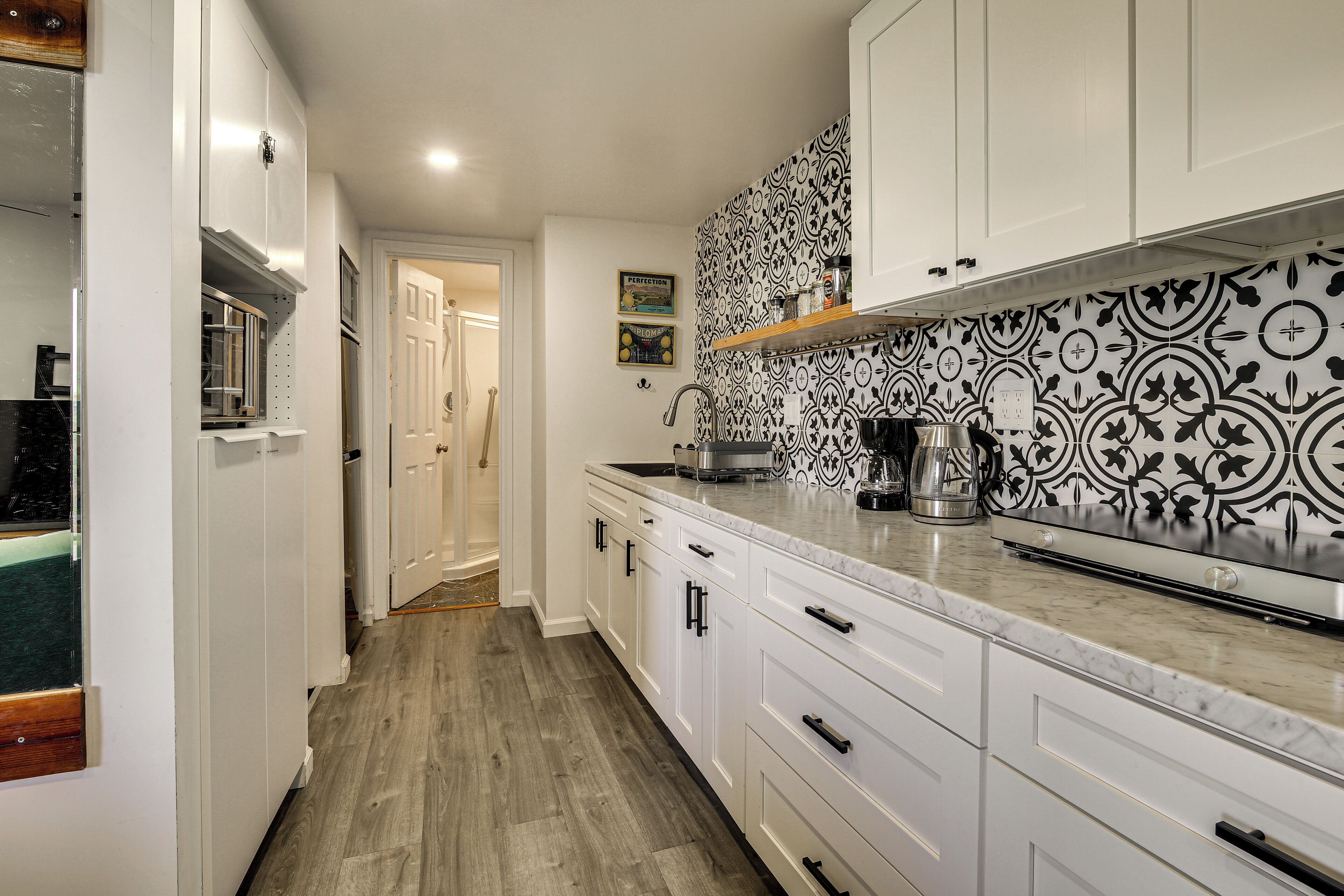 A kitchen with white cabinets, a patterned backsplash, and a wooden floor.
