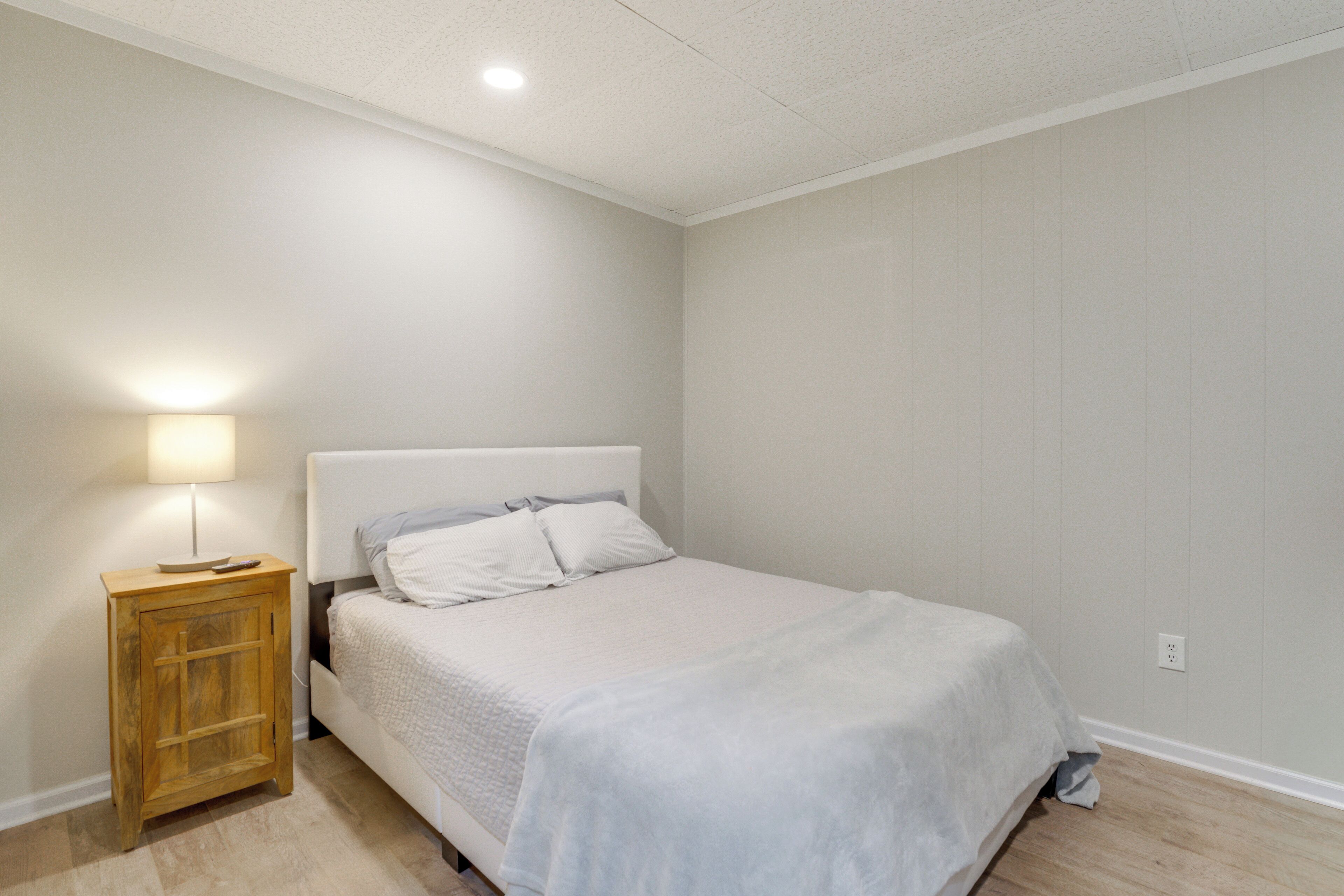 Een slaapkamer met een bed, nachtkastje, lamp en een plafondlamp.