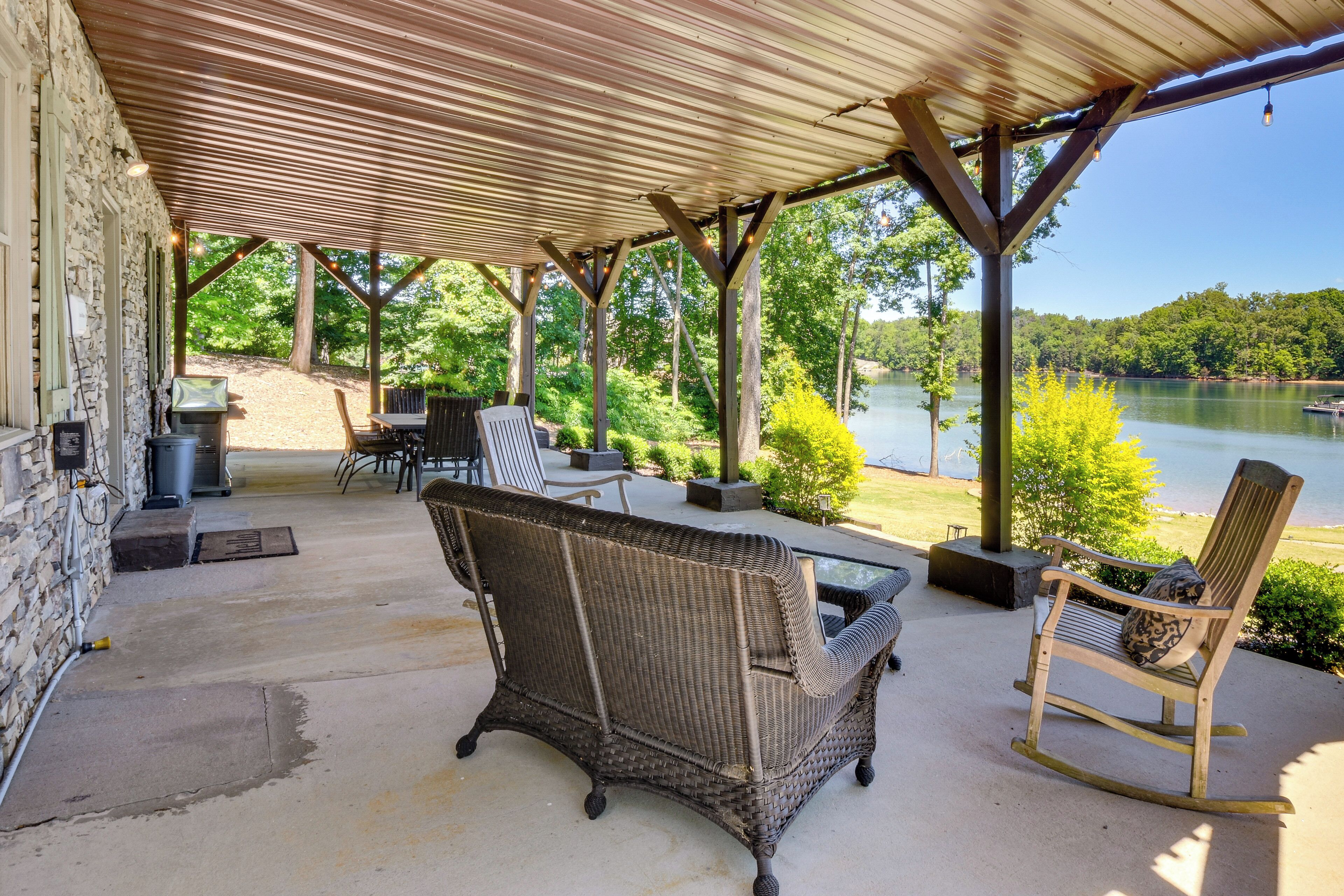 A covered patio with wicker furniture, a stone wall, and a view of a lake.