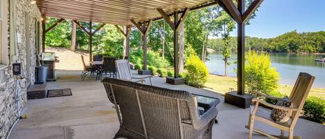 A covered patio with wicker furniture, a stone wall, and a view of a lake.