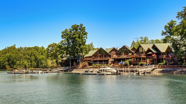 A lakeside lodge with multiple wooden cabins, docked boats, and a clear view of the lake. - Game Room, Dock & More! Panoramic Lakefront Oasis (Six Mile)