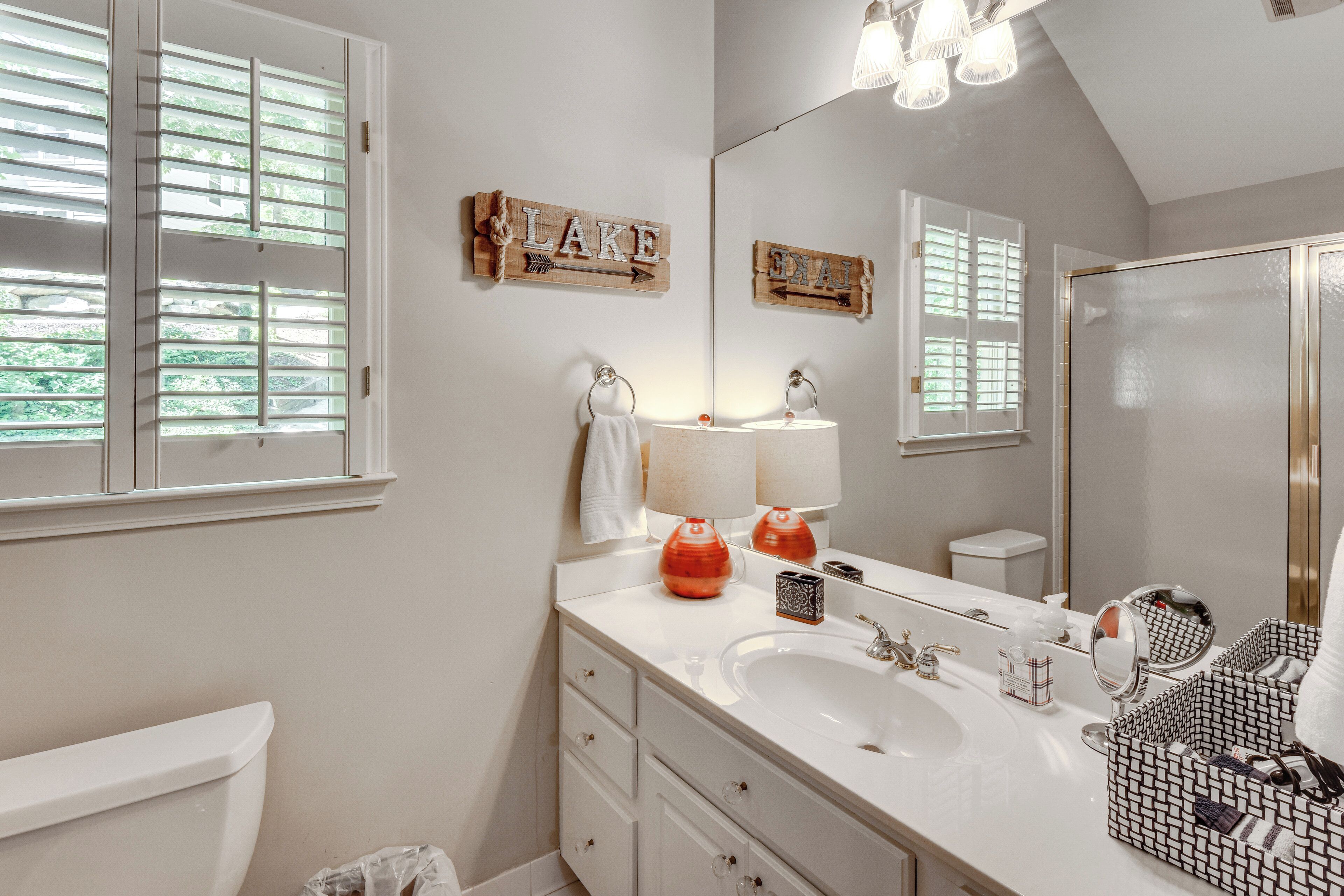 A bathroom with a white vanity, a large mirror, a sink, and a window with blinds.