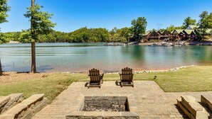 A lakeside patio with Adirondack chairs, a fire pit, and a lodge in the background. - Game Room, Dock & More! Panoramic Lakefront Oasis (Six Mile)
