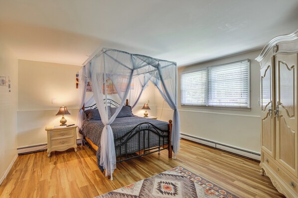 Un dormitorio con cama con dosel, lámparas de noche, mesitas de noche, alfombra estampada y un armario.