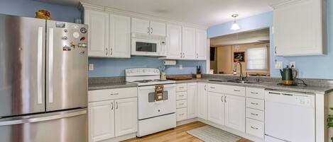 A modern kitchen with white cabinets, stainless steel appliances, and a wooden floor.