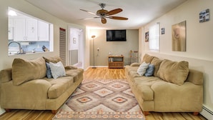 A living room with two beige sofas, a patterned rug, a ceiling fan, a TV, and a kitchen visible through an open door. - Trailside Escape! Cozy Stormville Apartment (Stormville)