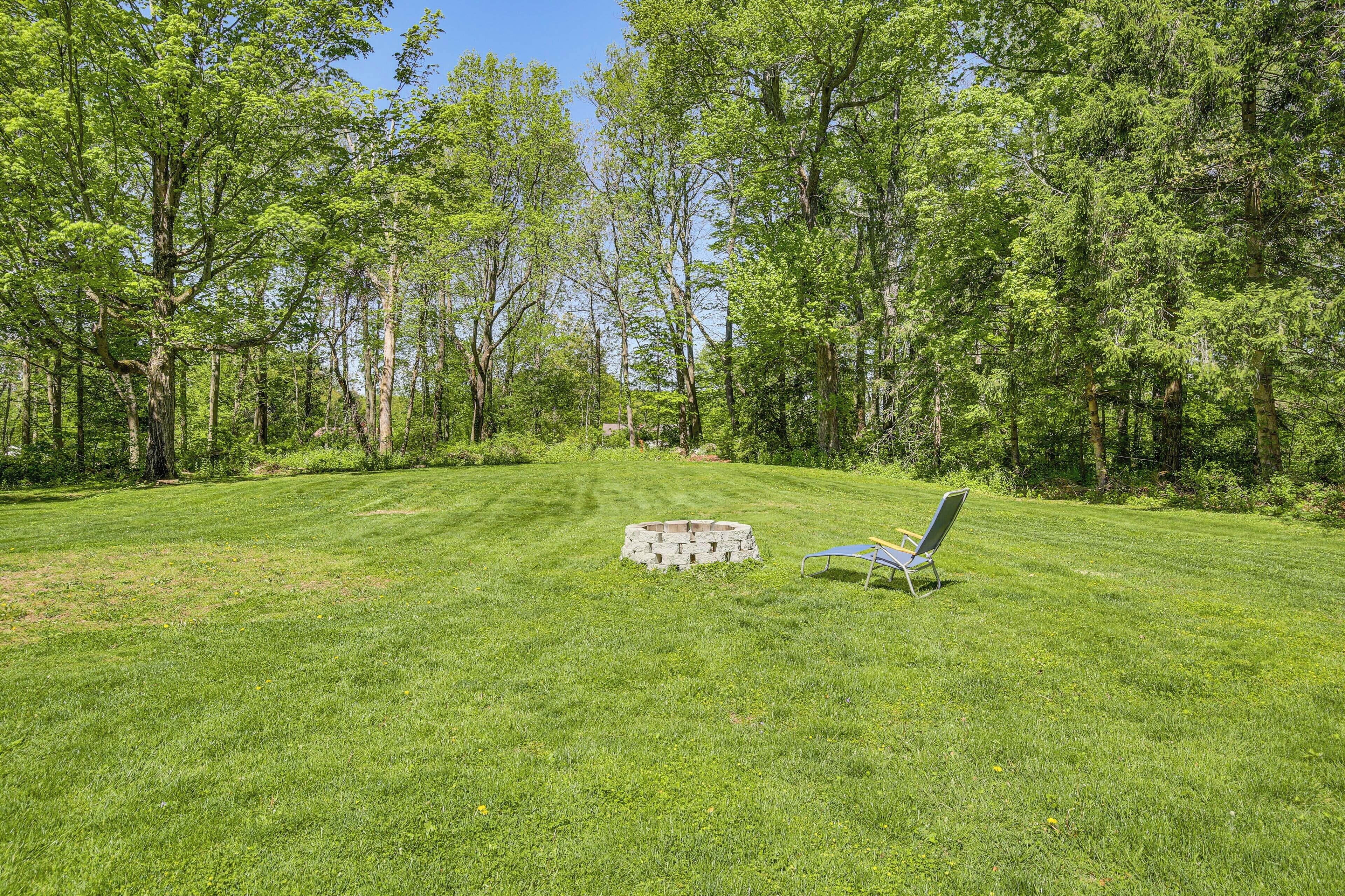 A grassy yard with a stone fire pit and a metal chair.