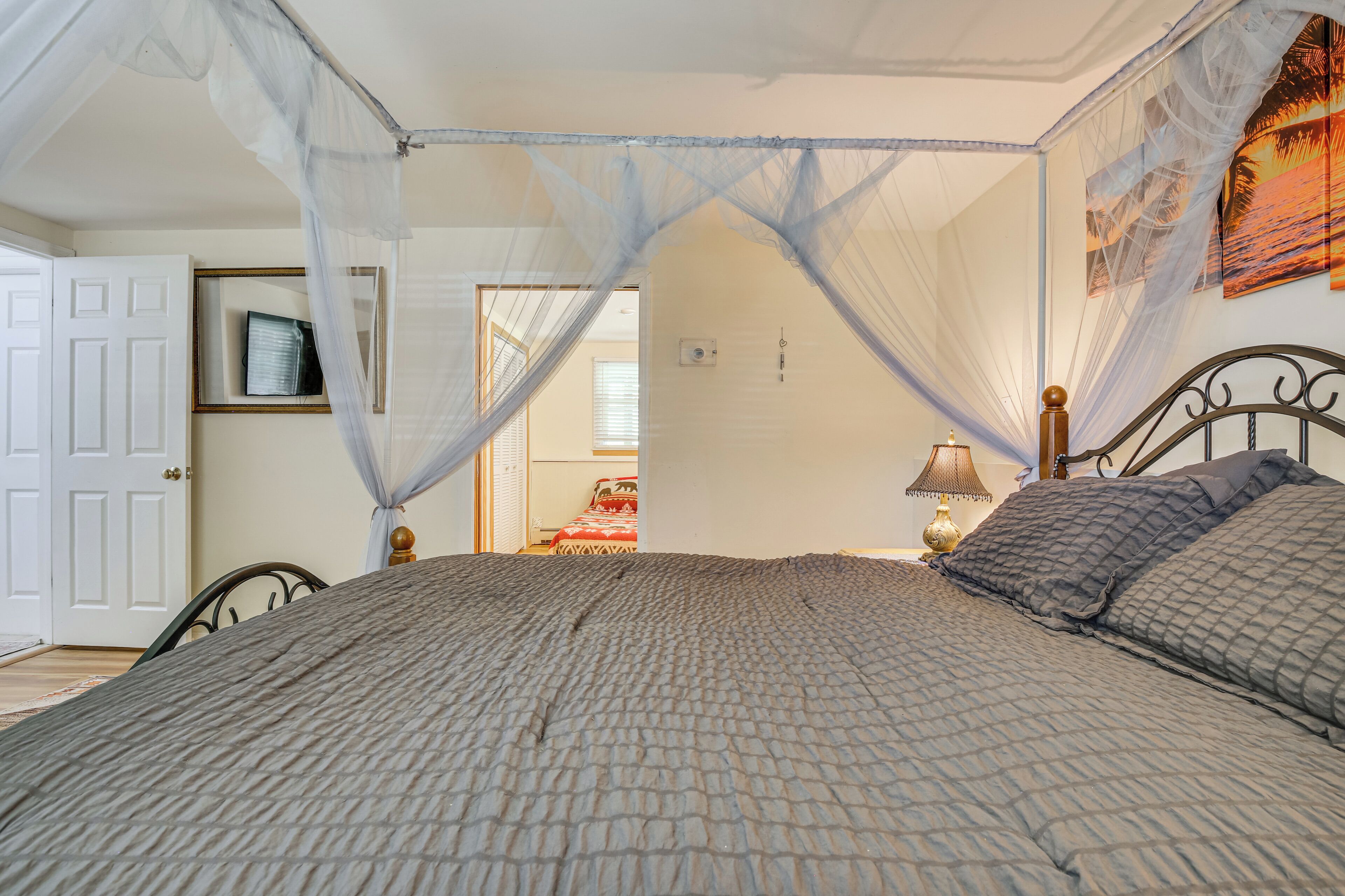 A bedroom with a bed, a nightstand, a lamp, a door, a framed picture, and a window.