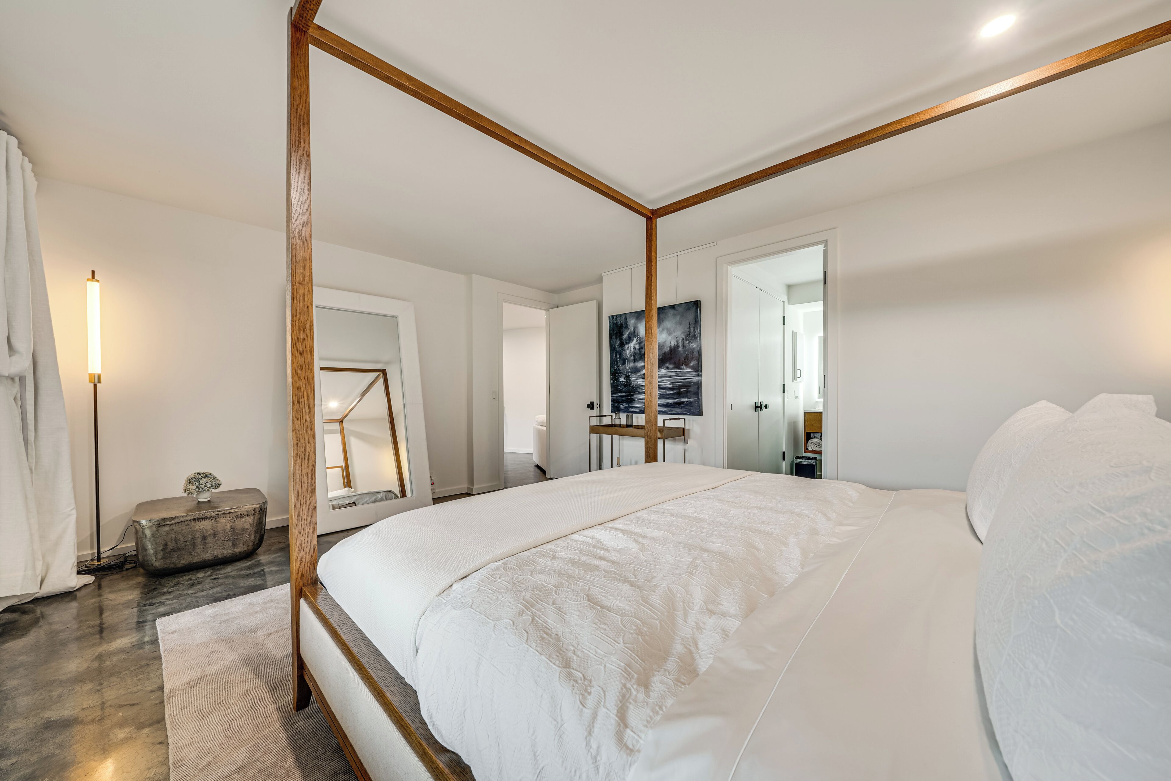Une chambre moderne avec un lit à baldaquin, une table de chevet, une lampe sur pied et un tableau au mur.