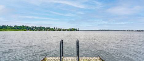 A boat with a patterned deck and two black poles, extending over calm water with a distant shoreline.