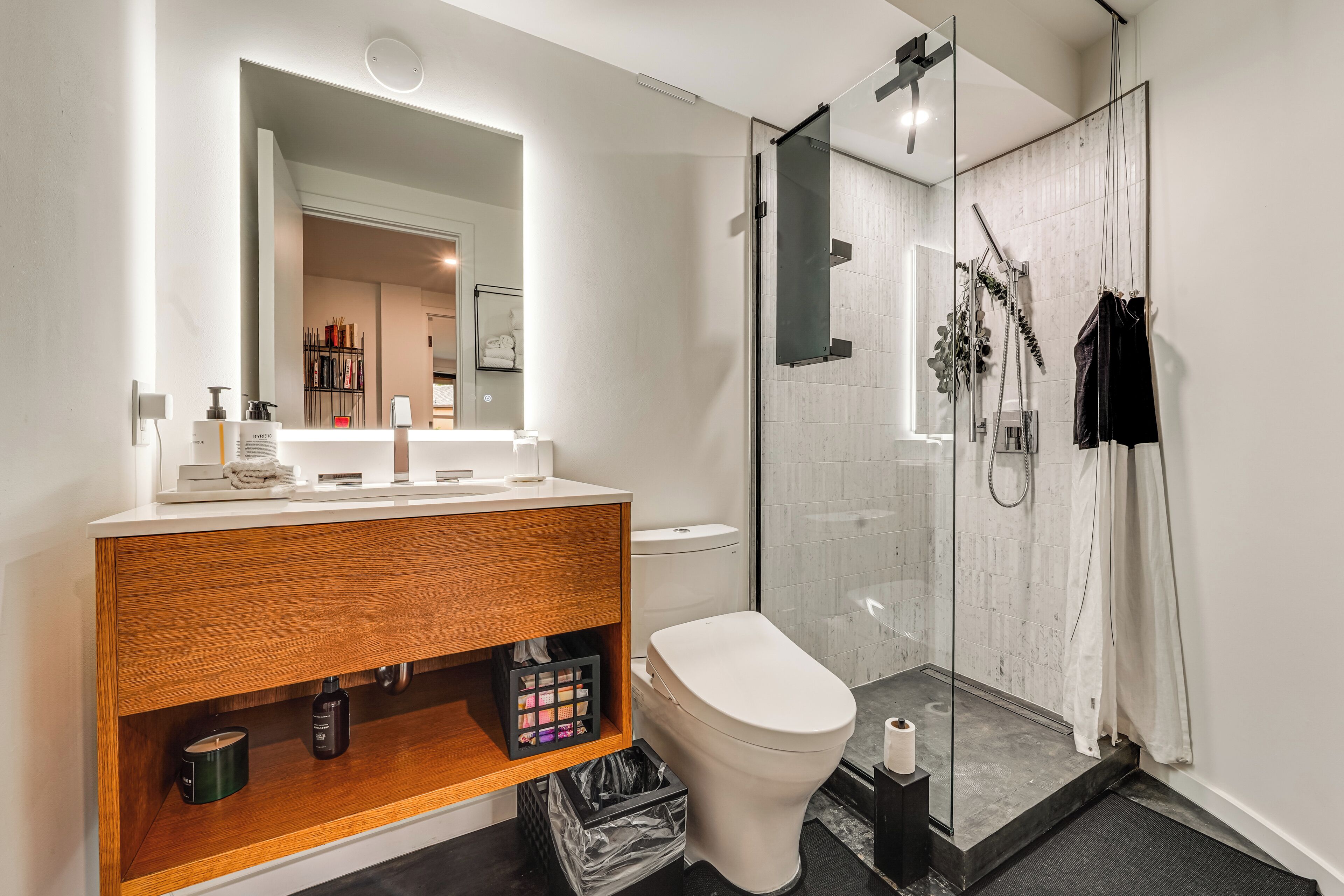 Une salle de bain moderne avec un meuble-lavabo en bois, des toilettes, une douche en verre et un grand miroir.
