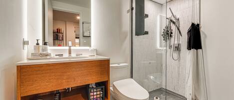 Une salle de bain moderne avec un meuble-lavabo en bois, des toilettes, une douche en verre et un grand miroir.