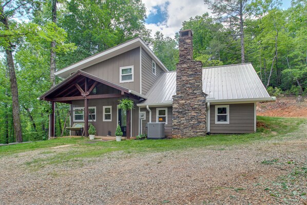 A two-story house with a stone chimney, a covered porch, and a gravel driveway.