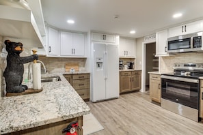 A modern kitchen with white cabinets, a stainless steel oven, a microwave, and a bear-shaped soap dispenser.