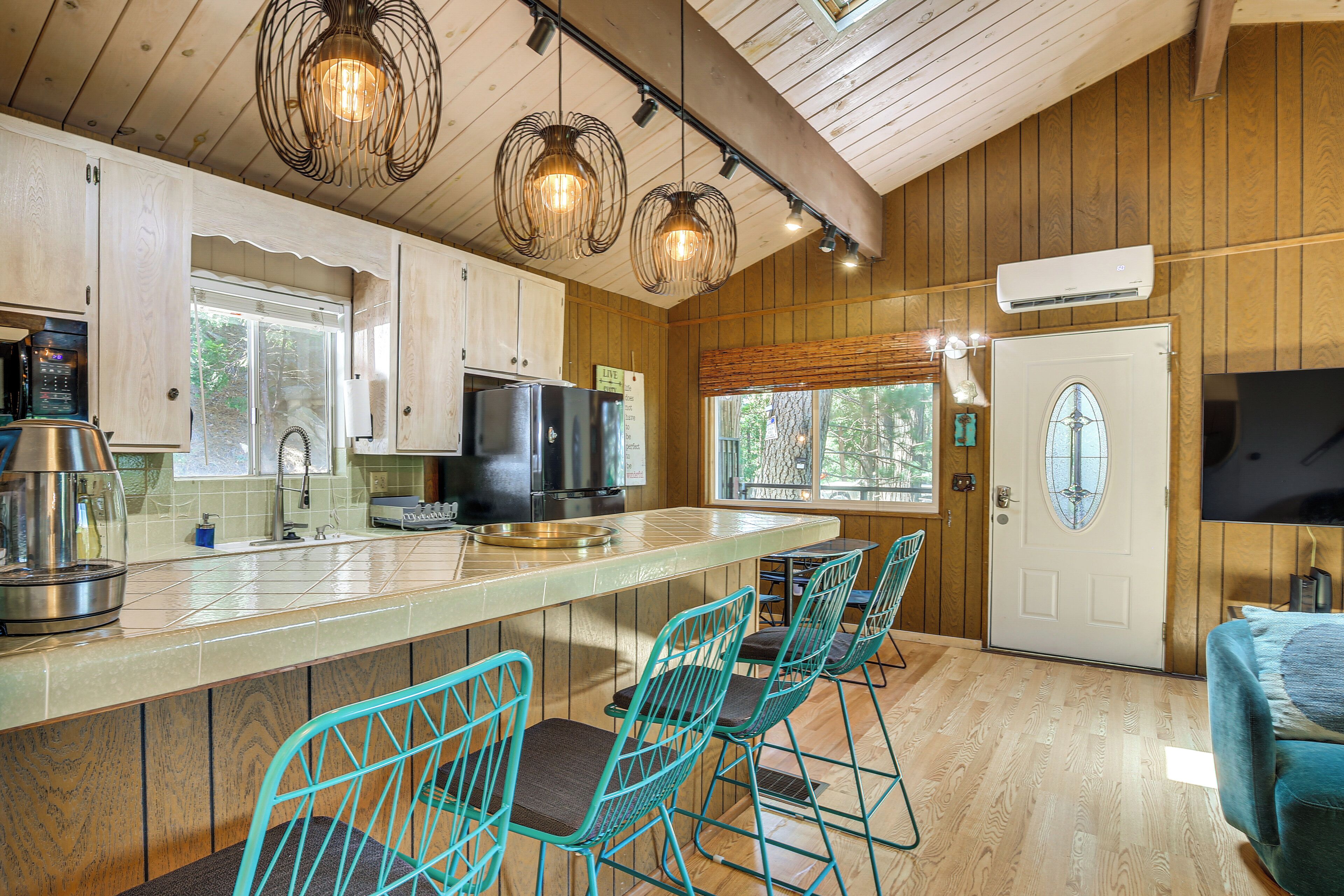 A kitchen with wooden cabinets, a stainless steel refrigerator, a large island with bar stools, and pendant lighting.
