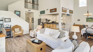 Un'ampia zona giorno con un divano bianco, una poltrona in vimini e un tavolo da pranzo con sedie. Una scala conduce a un piano superiore.