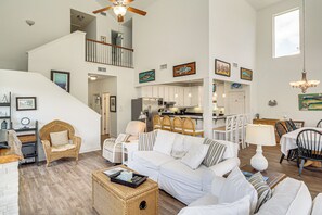 Ein geräumiger Wohnbereich mit weißem Sofa, Korbsessel und Esstisch mit Stühlen. Eine Treppe führt zu einer oberen Ebene.
