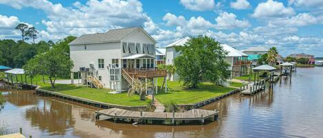 A waterfront property with a dock, a covered deck, and a house with a large deck and stairs leading to a second floor.