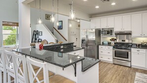 Una cucina moderna con mobili bianchi, piani di lavoro in granito, elettrodomestici in acciaio inossidabile e illuminazione a sospensione.