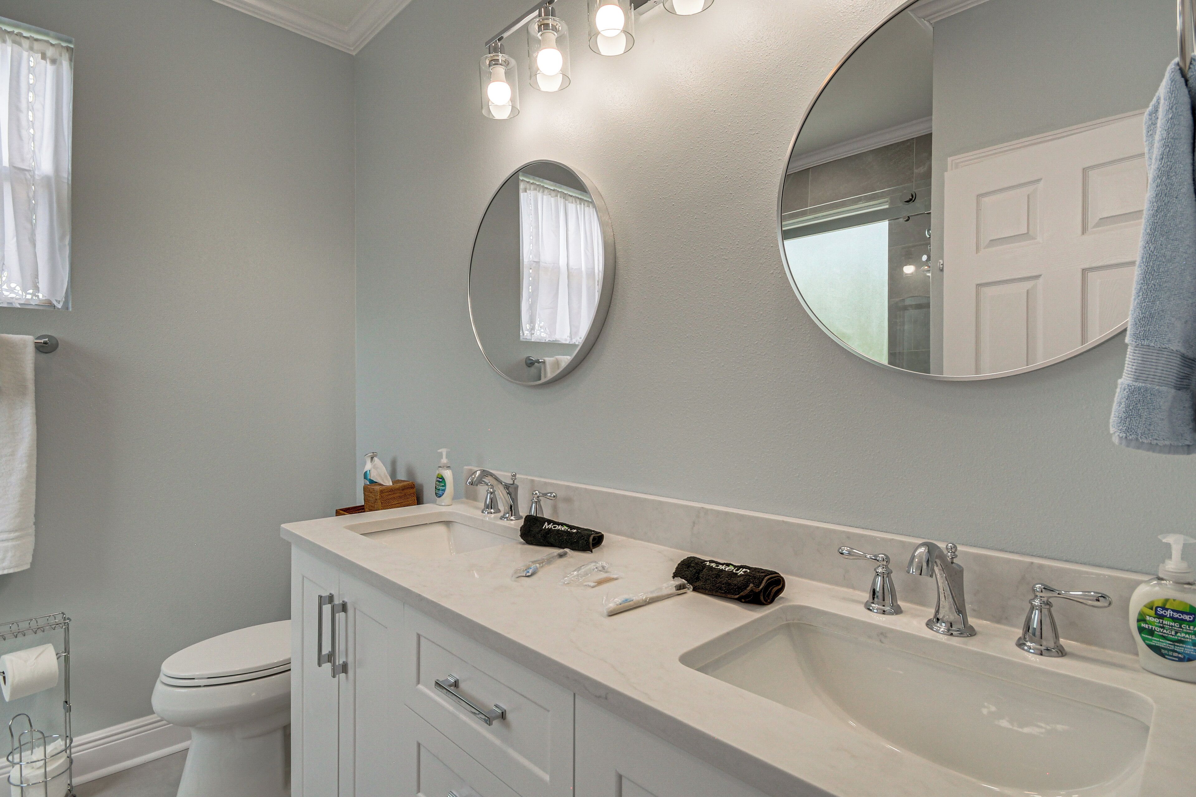 Une salle de bain avec un lavabo blanc, deux robinets, un miroir et un porte-serviettes.