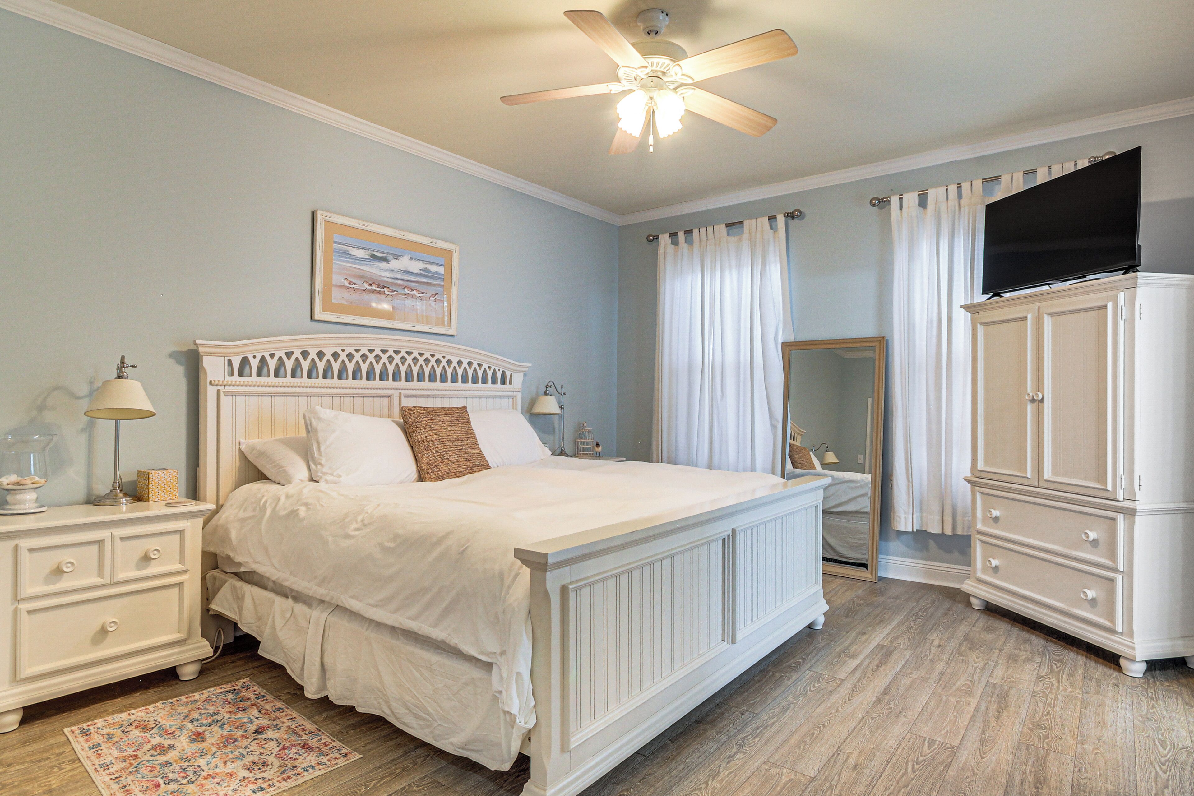 A bedroom with a bed, nightstands, a dresser, a ceiling fan, and a mirror.