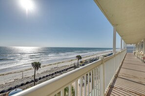 Blick auf den Strand von einem überdachten Balkon mit Holzdeck und weißen Geländern.