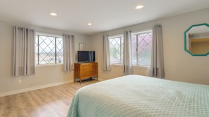 A bedroom with a bed, a TV on a wooden dresser, and two windows with curtains. - Creekside Picnic Area! Stay Near Blue Water Bridge (Port Huron)