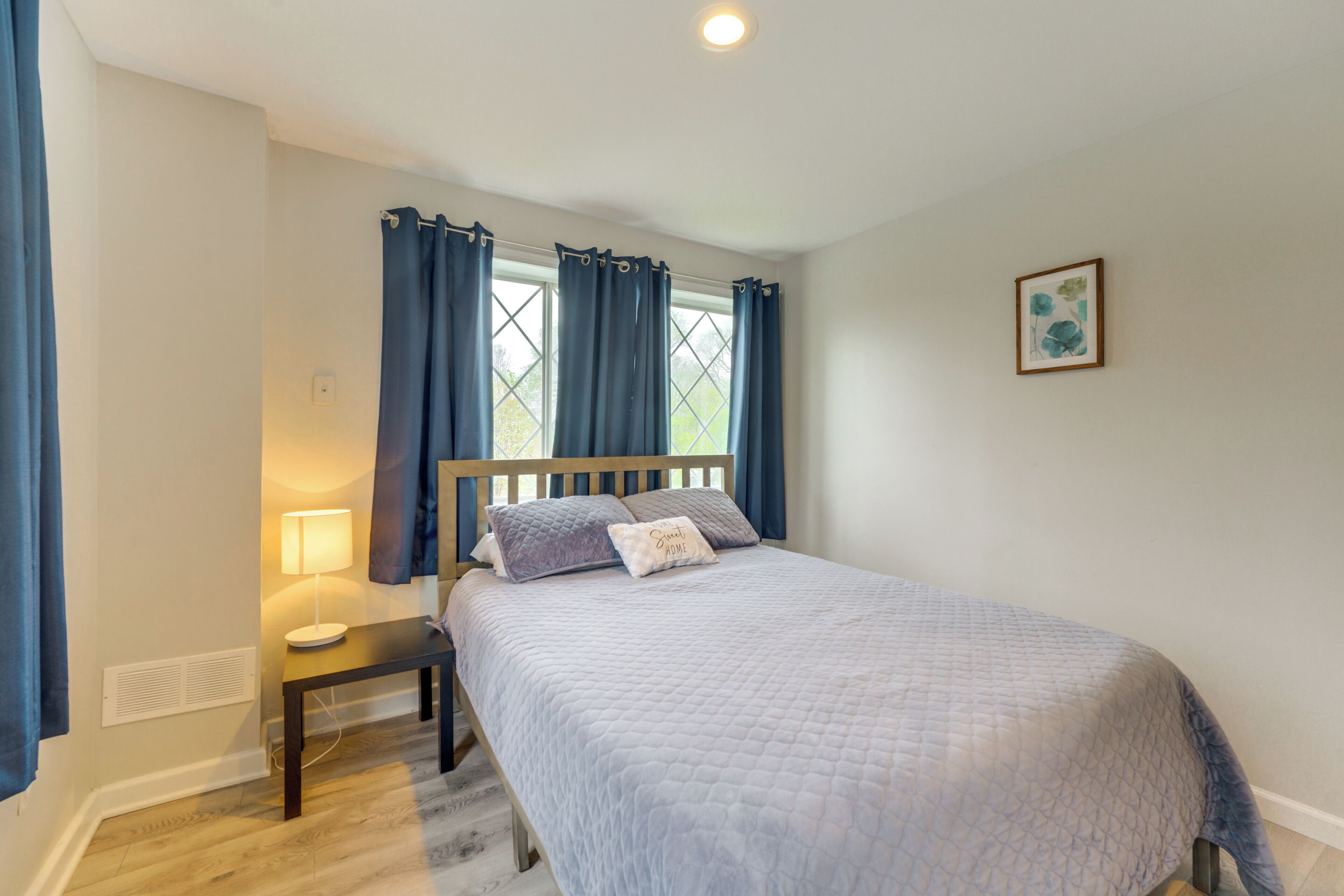 Un dormitorio con cama, mesita de noche, lámpara y ventana con cortinas.