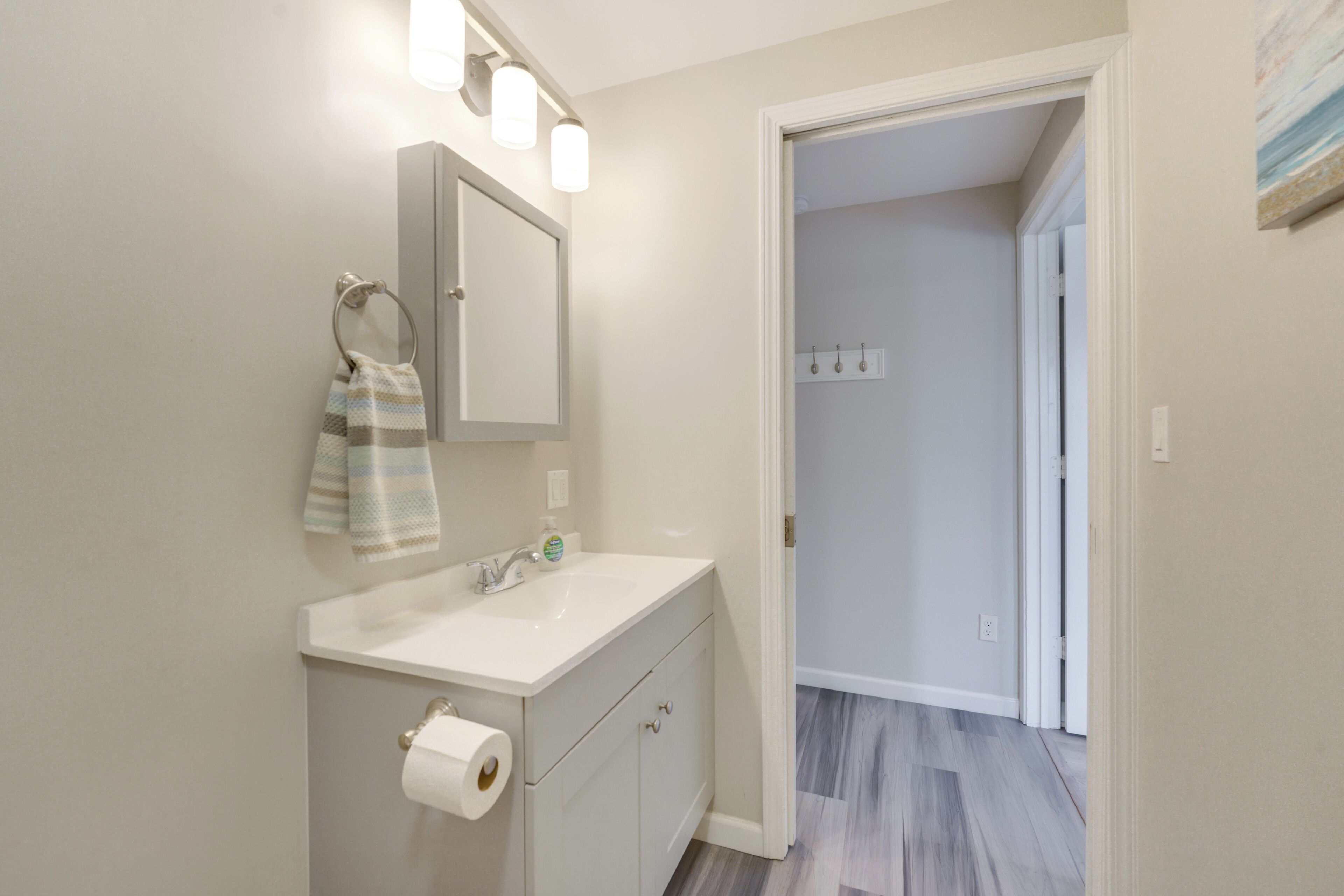 A bathroom with a white vanity, a mirror, a towel rack, and a toilet paper holder.