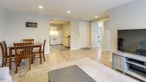 A living room with a dining table, chairs, a sofa, a TV stand, and a kitchen in the background. - Creekside Picnic Area! Stay Near Blue Water Bridge (Port Huron)