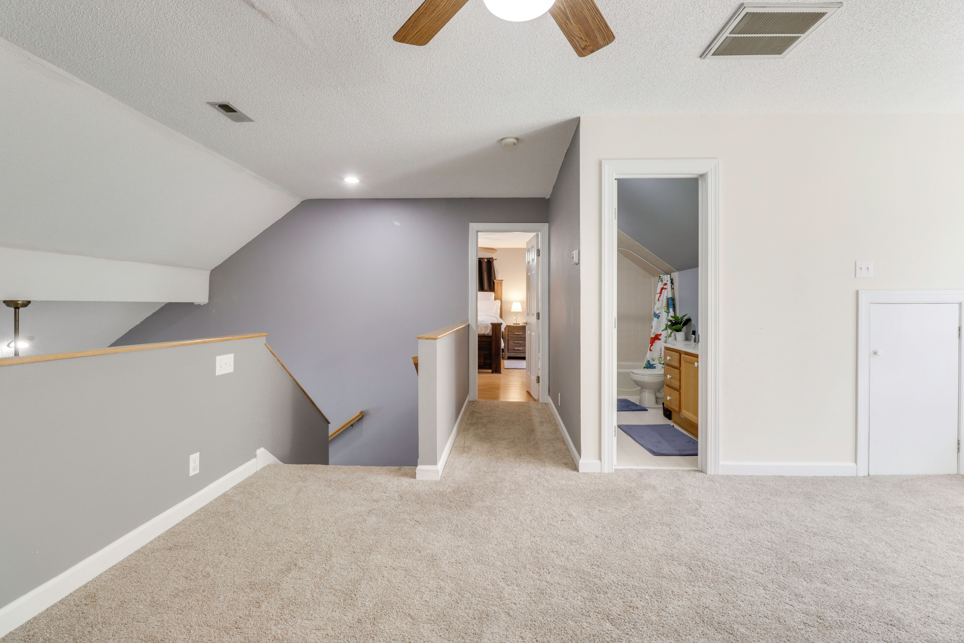 A hallway with a carpeted floor, a ceiling fan, and a staircase leading to another room.
