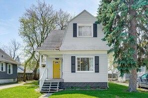 Uma casa térrea com varanda frontal, porta amarela e pequeno jardim da frente.
