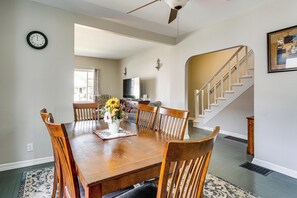 A dining area with a wooden table, chairs, a vase with flowers, a clock on the wall, and a staircase leading to another level. - Gateway to Dtwn Port Huron & Lake! Cozy Home (Port Huron)