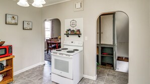 A kitchen with a white stove, a microwave on a wooden shelf, and a wall-mounted shelf with food items. - Gateway to Dtwn Port Huron & Lake! Cozy Home (Port Huron)