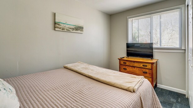 A bedroom with a bed, a dresser, a television, a window with blinds, and a painting on the wall. - Gateway to Dtwn Port Huron & Lake! Cozy Home (Port Huron)