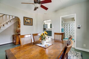 Uma sala de jantar com mesa de madeira, cadeiras, ventilador de teto e uma escada.