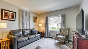 A living room with a leather sofa, patterned armchair, and a flat-screen TV on a wooden cabinet. - Gateway to Dtwn Port Huron & Lake! Cozy Home (Port Huron)