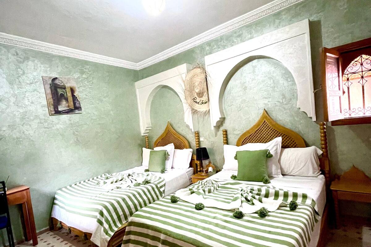 A room with two beds, a small table, a decorative ceiling light, and a wall-mounted picture.