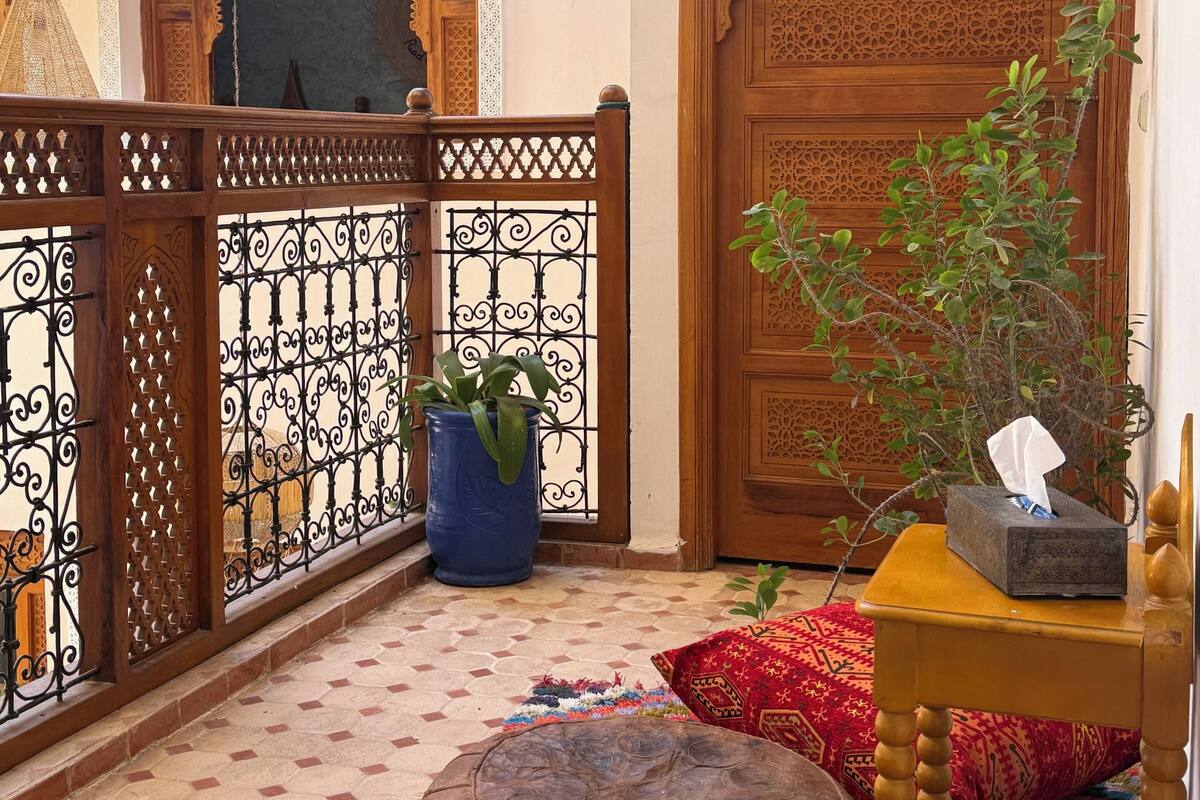 A traditional Moroccan interior with a wooden door, a hanging lantern, a potted plant, and a colorful rug.
