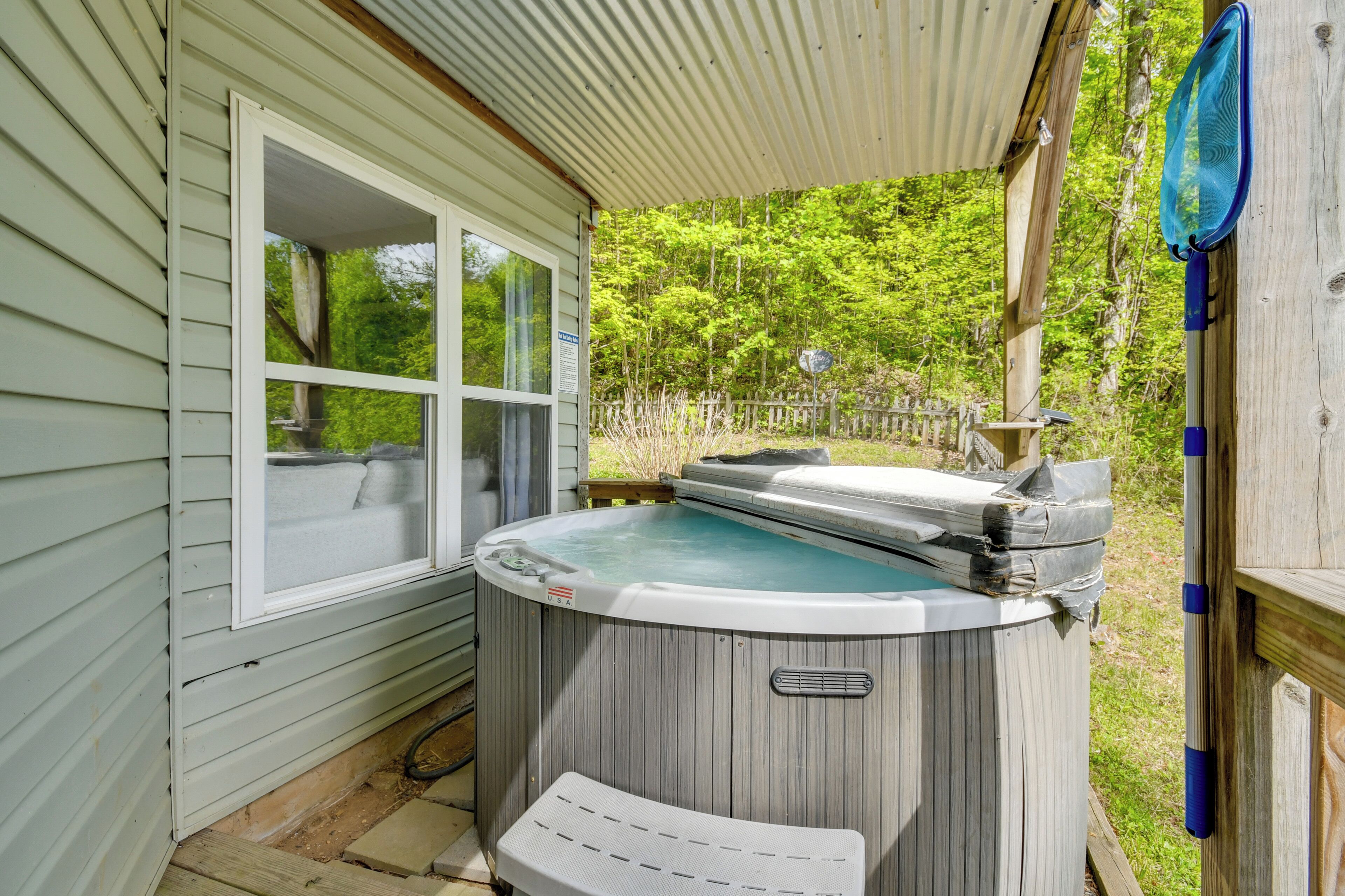 A hot tub outside a house with a wooden deck, a window, and a fence in the background.