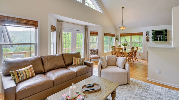 A spacious living room with a brown leather sofa, a beige armchair, a wooden coffee table, and a dining area with a table and chairs. - Mountain Views & Hot Tub - Your Blue Ridge Getaway (Barnardsville)