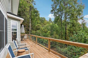 A wooden deck with chairs and a table, surrounded by a metal railing, overlooking a forested area. - Mountain Views & Hot Tub - Your Blue Ridge Getaway (Barnardsville)