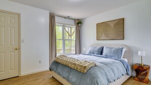 A bedroom with a bed, a window with curtains, a bedside table with a lamp, and a wall-mounted artwork. - Mountain Views & Hot Tub - Your Blue Ridge Getaway (Barnardsville)
