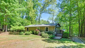 A single-story house with a front porch, surrounded by a well-maintained lawn and dense trees. - Dock & Pavilion! Lake Norman Retreat on Quiet Cove (Mooresville)